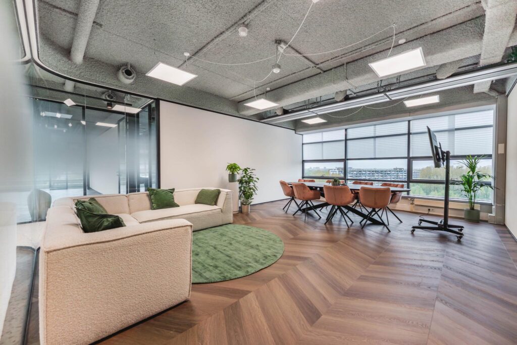 Modern office space on Joop Geesinkweg with a lounge area, meeting table, and large windows offering natural light.